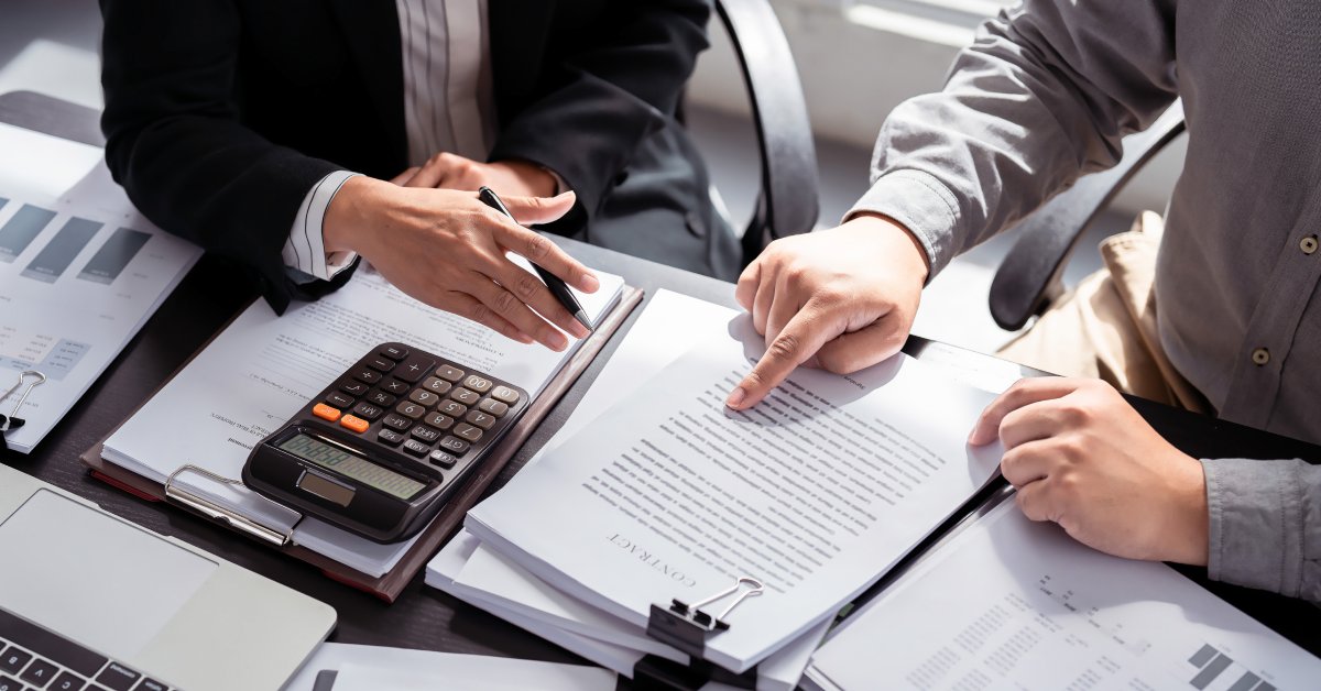 An overhead view of two men in business attire reviewing documents on a desk with clipboards and calculators.