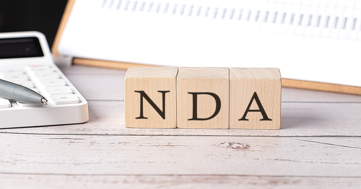 A close-up of three wooden blocks with letters printed on them that say "NDA" next to a calculator and clipboard.